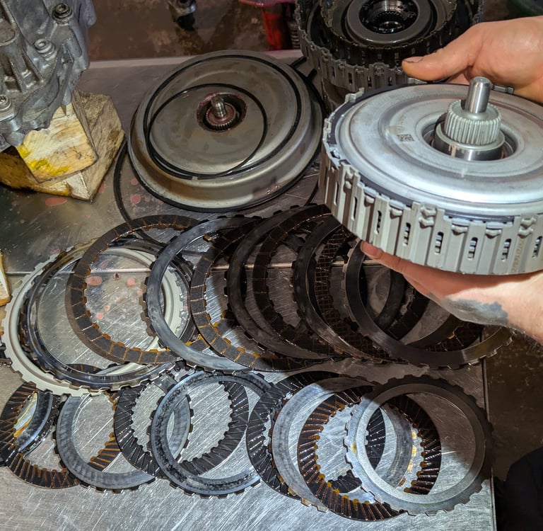 A mechanic holding a dual clutch assembly over a set of metal friction discs on a workbench.
