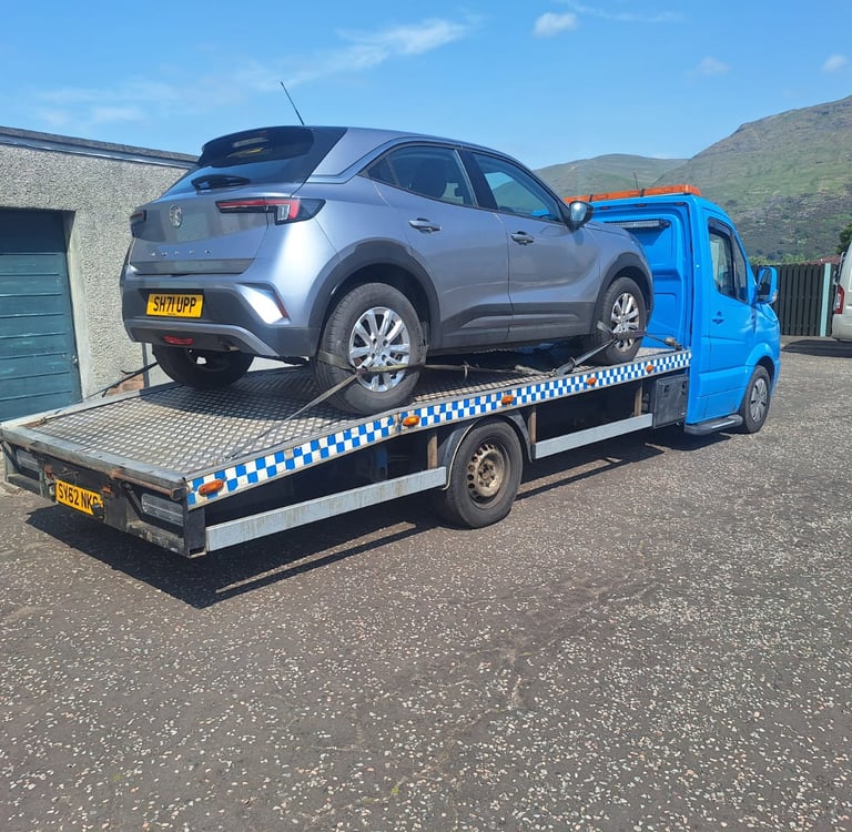 A silver Vauxhall Mokka car being transported on a blue flatbed recovery tow truck.