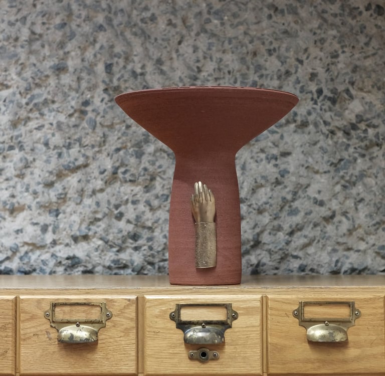 Tall ceramic vessel in deep red stoneware, with a bronze sculpted hand mounted on the base.