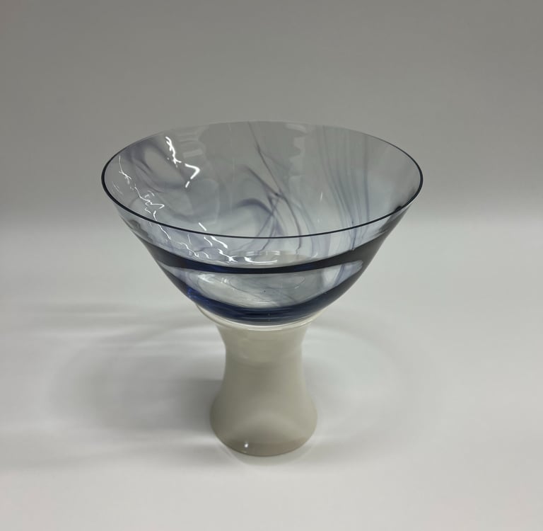 Large and wide blown glass bowl, with swirls of ink blue glass, on a white porcelain ceramic base. 