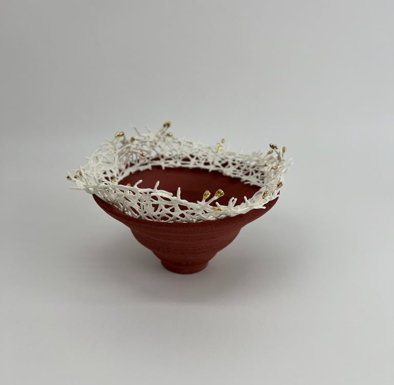 A thrown stoneware ceramic tiered bowl, topped with a porcelain white crown sculpture, tipped gold