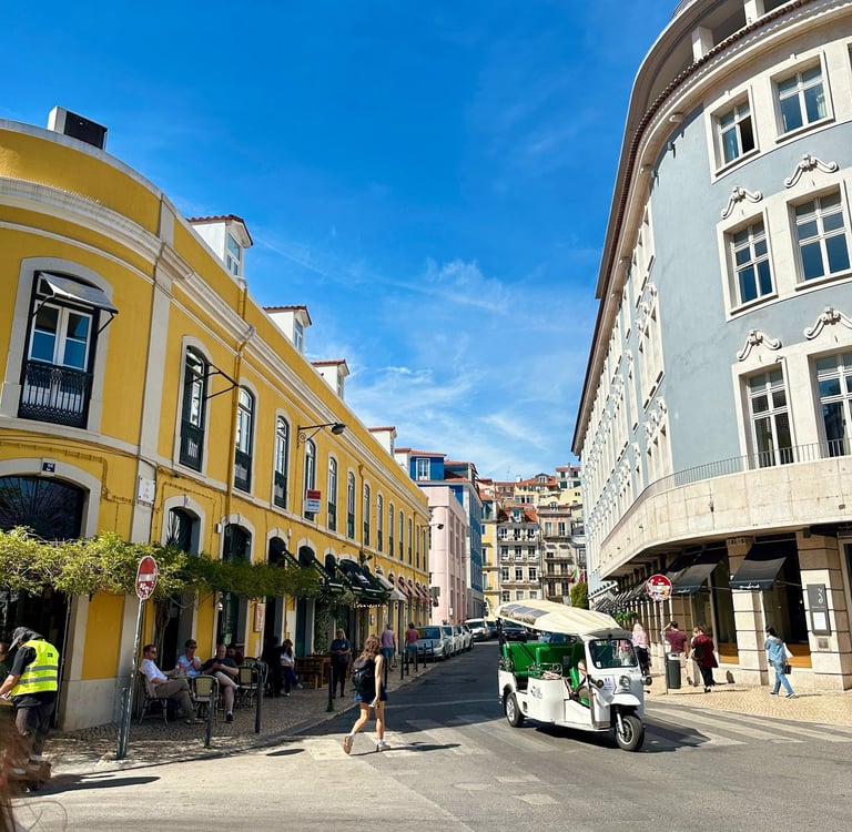 Prédios, um estrada, pessoas em bares e um tuk tuk