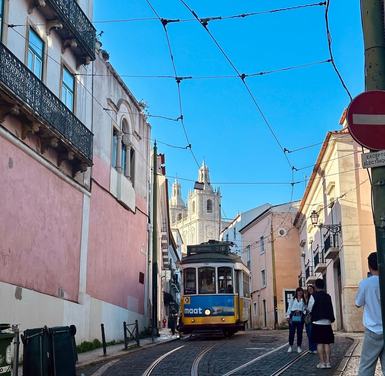 Uma estrada estreira entre as casas portuguesas, com um bondinho ao meio e a catedral ao fundo.