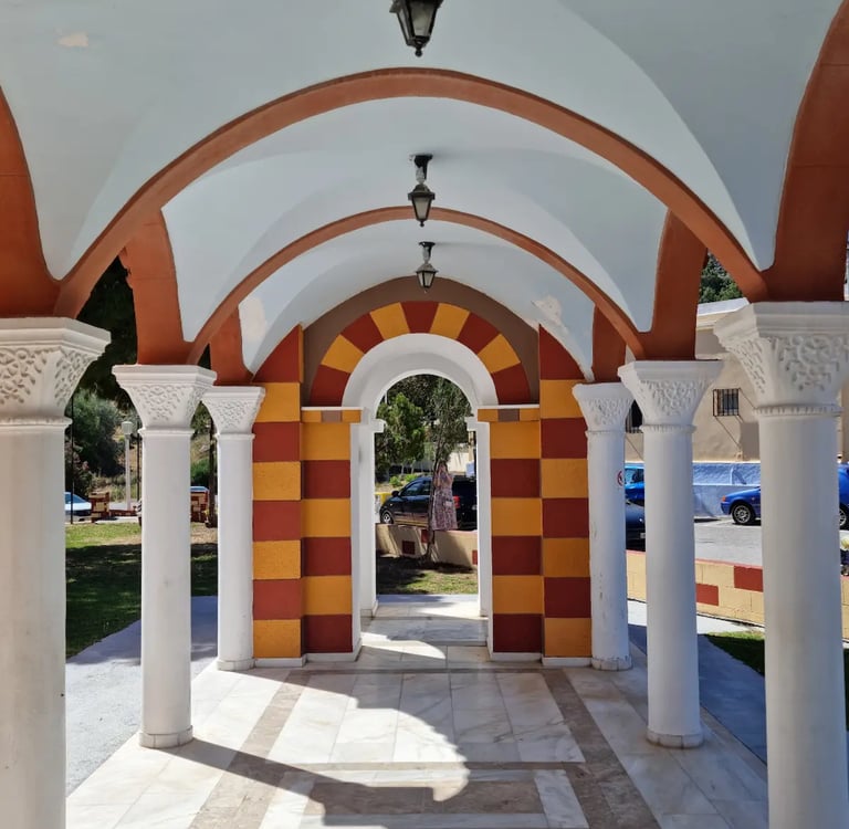 Greek Orthodox church arcade with white marble columns and arched hallways in a sunny courtyard.