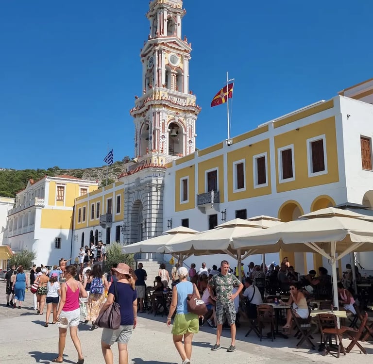 Panormitis Monastery clock tower and courtyard with tourists on Symi Island, Greece.