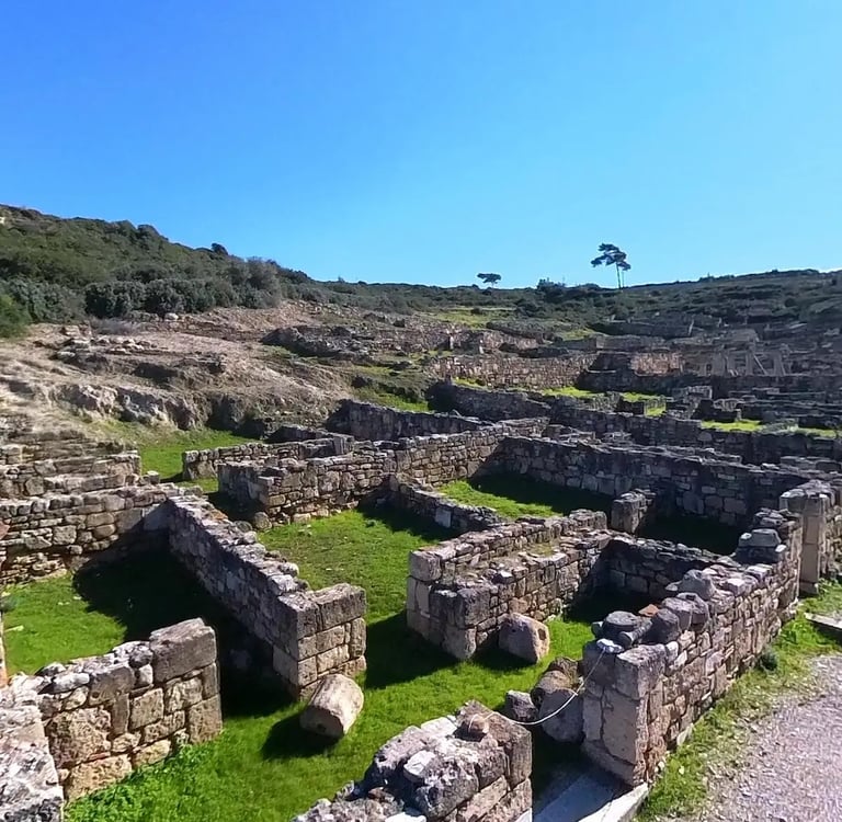 Ancient stone ruins of the city of Kamiros in Rhodes, Greece, under a clear blue sky.