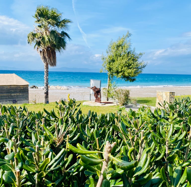 Tropical beach landscape with green shrubs, palm trees, and a historic cannon overlooking the blue sea.