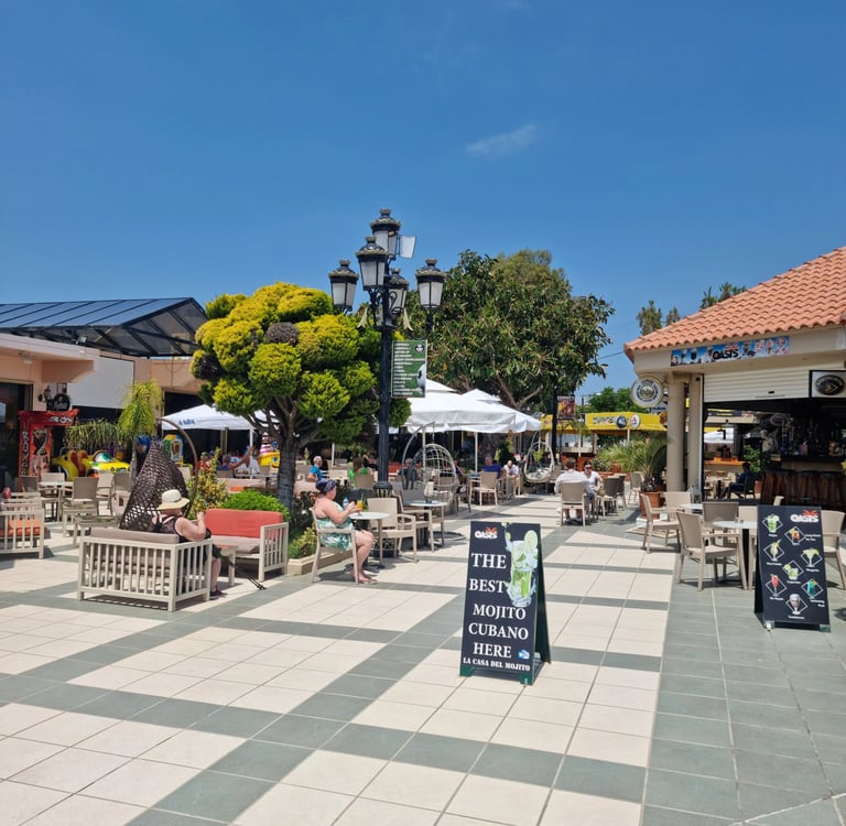 Sunny outdoor patio at a resort with people relaxing at café tables under a blue sky.