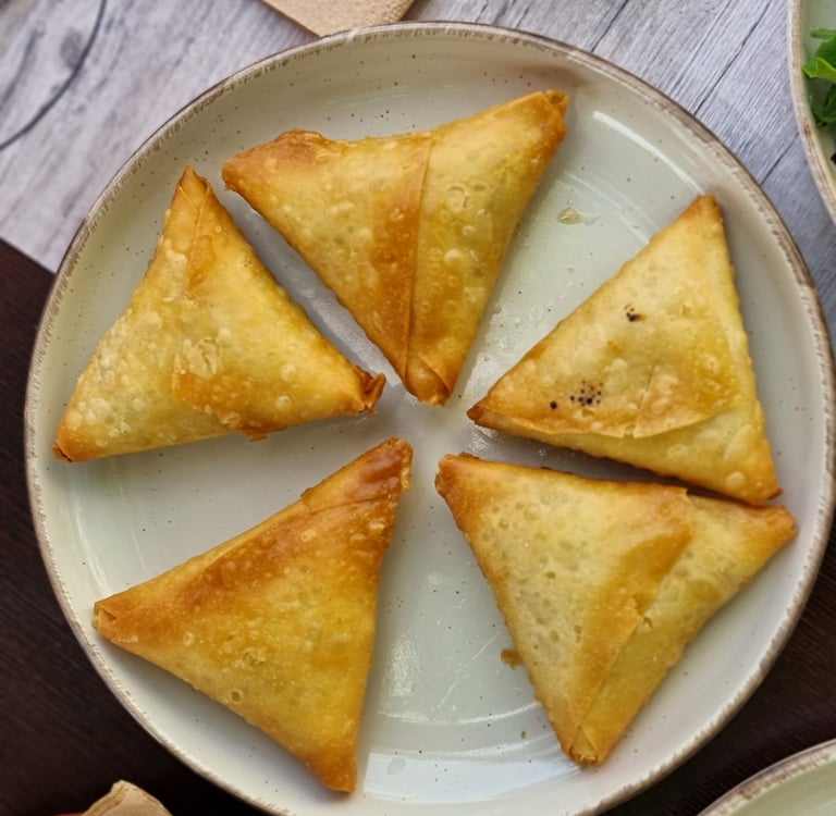 A plate of five golden-brown, crispy triangular vegetable samosas arranged in a circle.