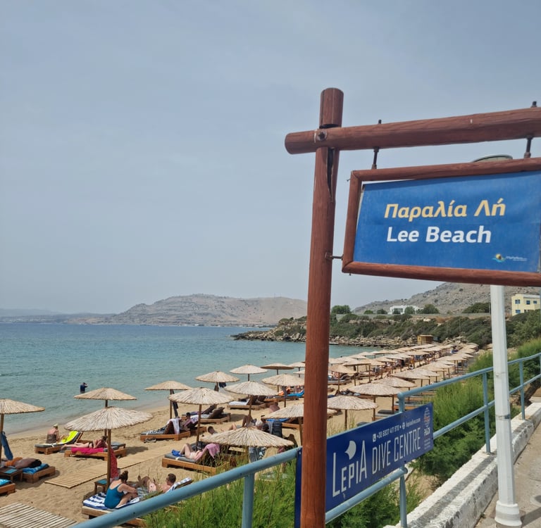 Lee Beach in Rhodes, Greece, with straw umbrellas and blue signs overlooking the Aegean Sea.