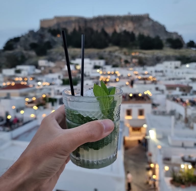 A refreshing mint mojito cocktail at a Lindos rooftop bar with the Acropolis of Rhodes in the background.