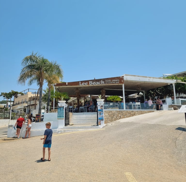 Lee Beach Food, Drinks & Cocktail Bar on a sunny day with patrons and palm trees.