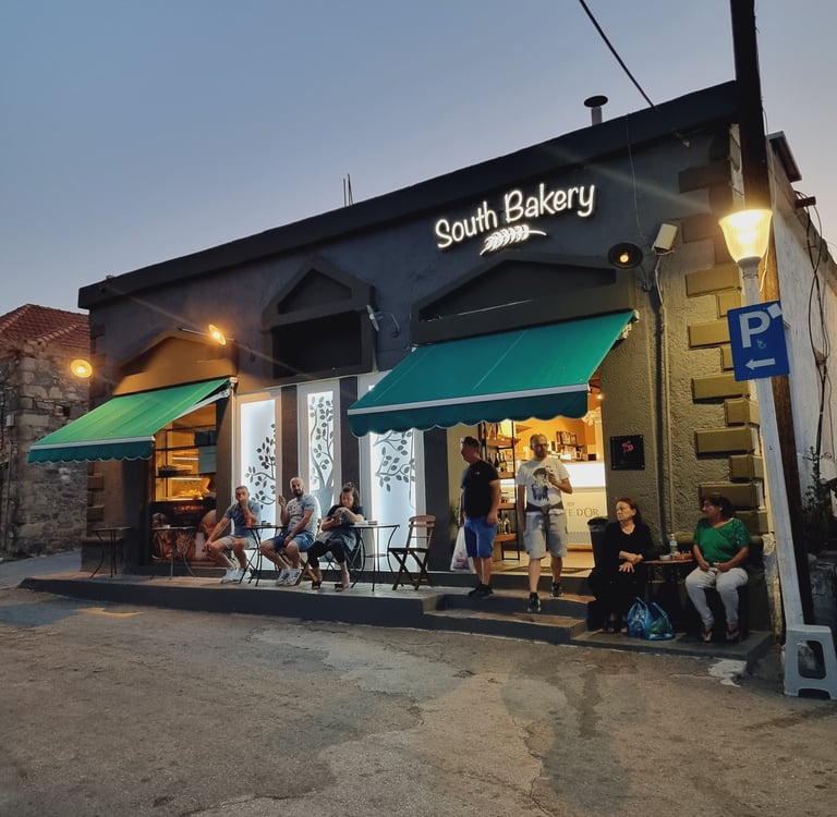 Customers relax outside South Bakery, a modern storefront with green awnings and outdoor seating at twilight.