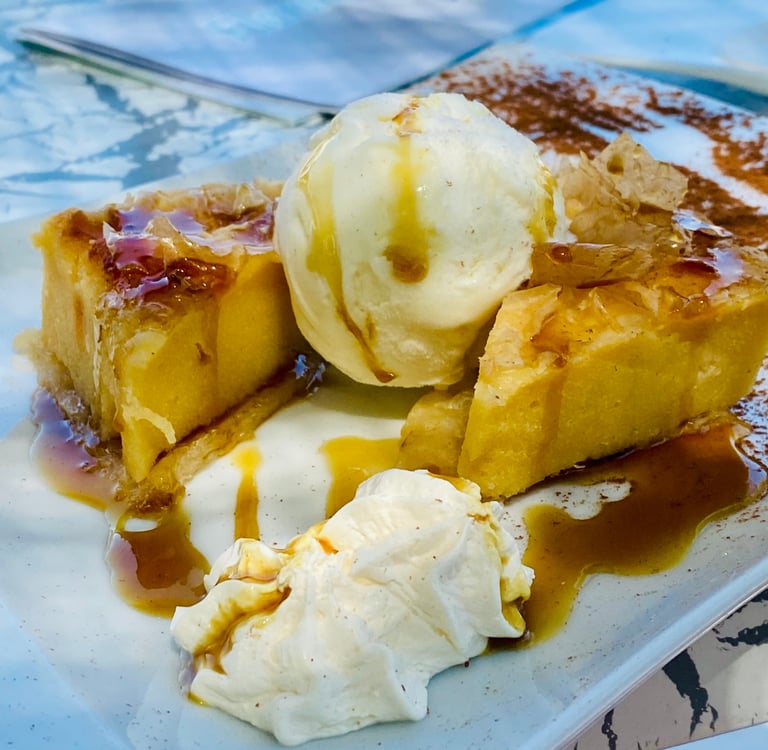 Warm Greek orange cake served with vanilla ice cream and honey syrup on a white plate.