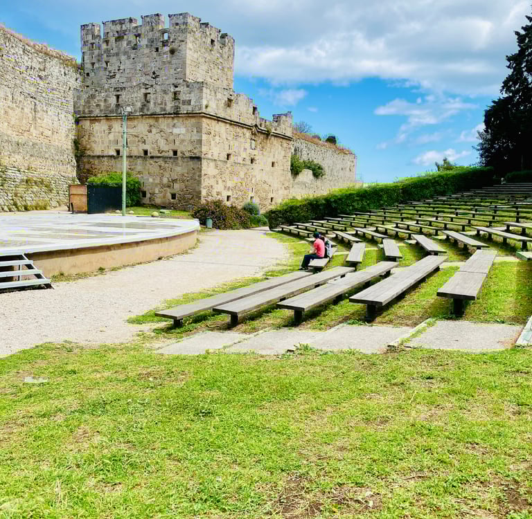 Outdoor stone amphitheater and historic medieval fortress walls in Rhodes, Greece under a blue sky.