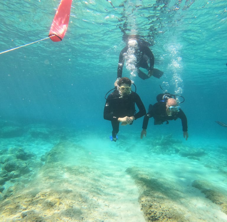 Scuba divers exploring clear blue tropical waters over a rocky seafloor with coral reefs.