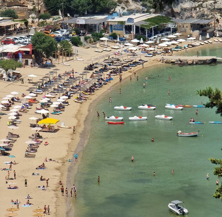 Aerial view of a crowded Mediterranean beach with rows of umbrellas and boats in the turquoise sea.