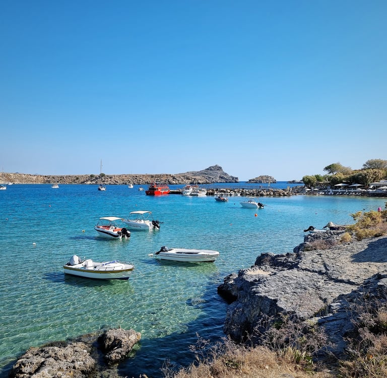 Scenic bay with crystal clear turquoise water, small boats, and a rocky coastline under a bright blue sky, ideal for summer