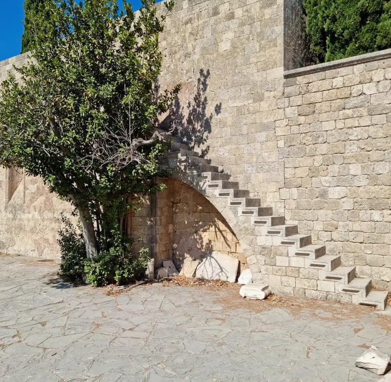 Ancient stone steps built into a medieval fortress wall next to a green tree in Rhodes, Greece.