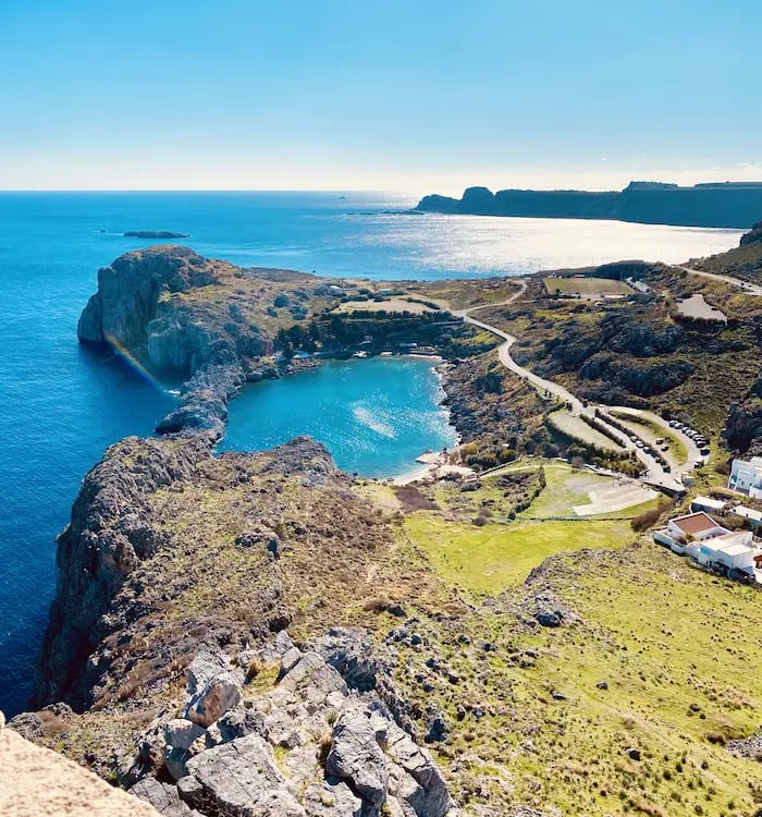 Aerial view of St: Paul's Bay in Lindos, Rhodes, featuring turquoise waters and rocky Greek coastline.