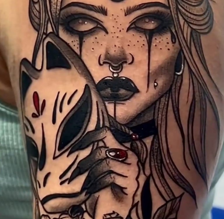 Detailed black and grey ink tattoo on shoulder featuring a gothic woman with a crescent moon and kitsune mask.