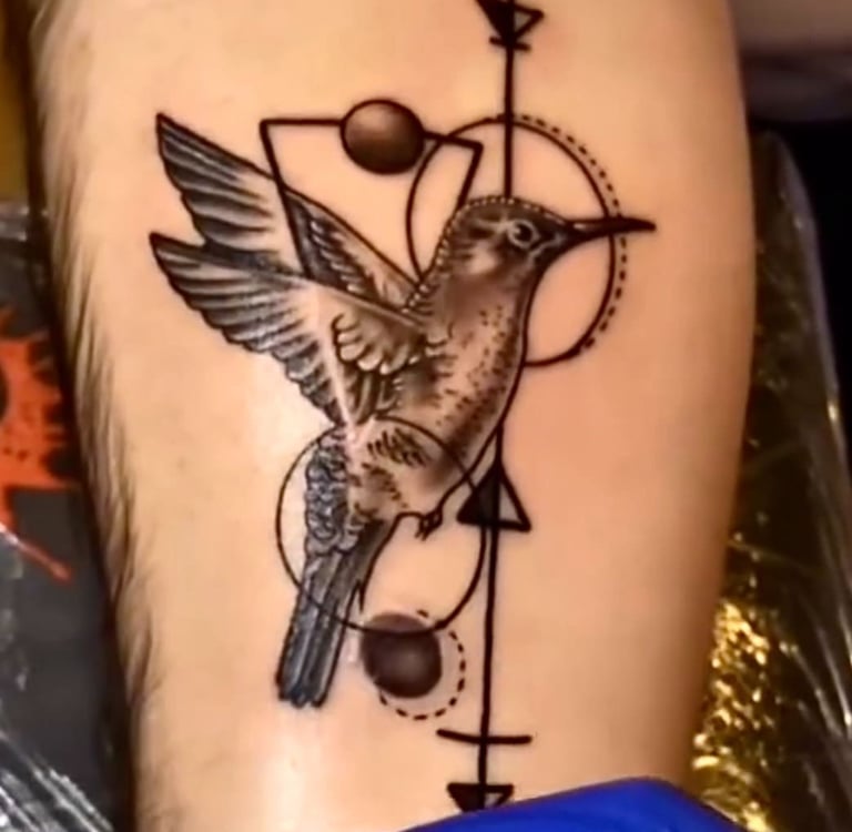 Detailed black and grey hummingbird tattoo with geometric shapes and lines on a forearm.
