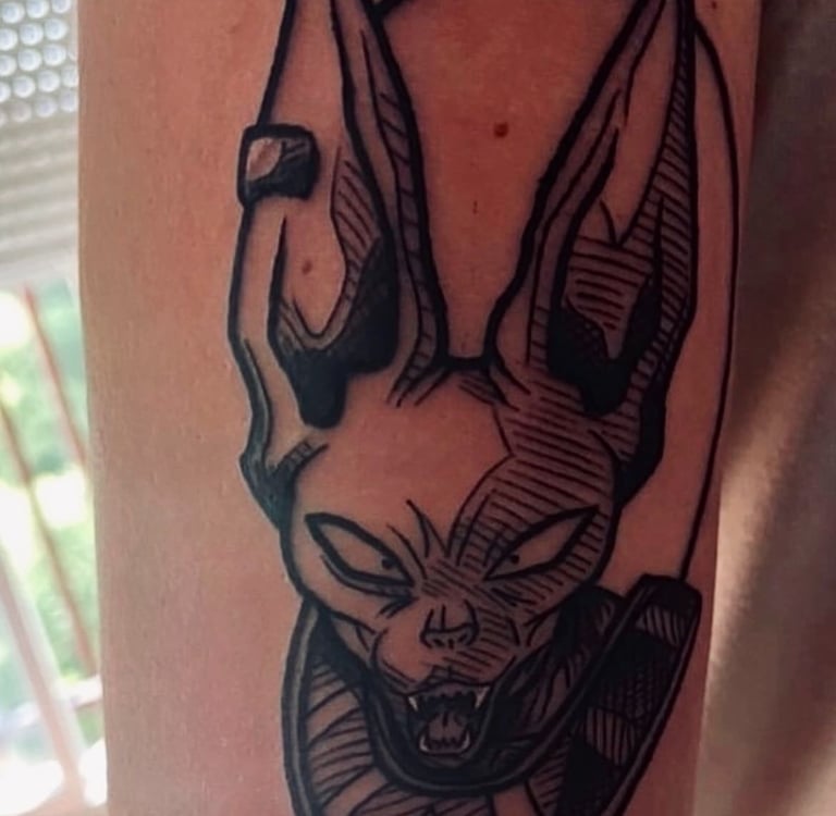 A detailed black and white tattoo of Beerus, the God of Destruction from Dragon Ball Super, with his signature smirk and