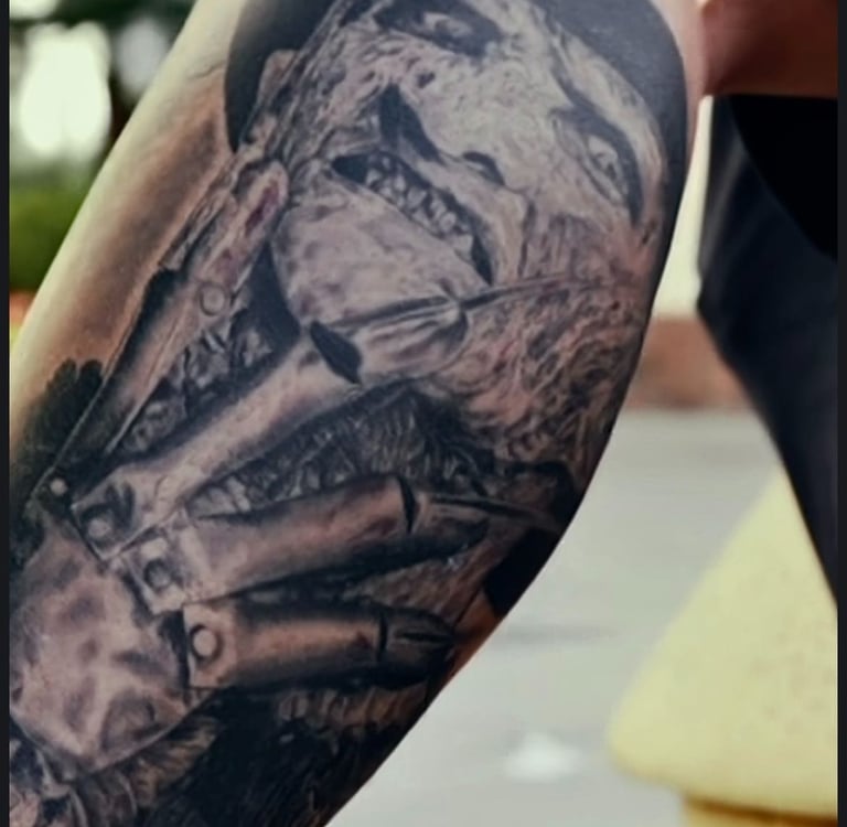 Realistic black and grey Freddy Krueger tattoo on an arm featuring his iconic bladed glove and burnt face.