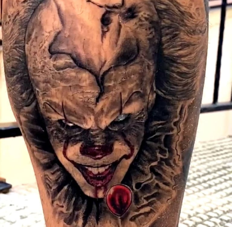 A realistic black and grey Pennywise the clown tattoo with a red balloon on a person's leg.