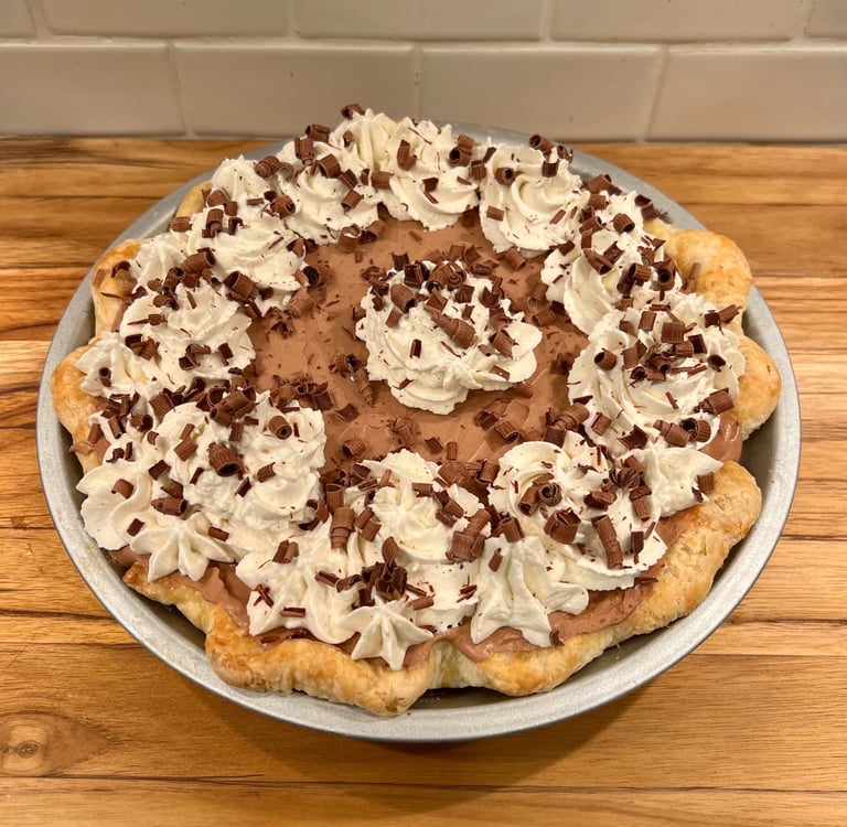 A homemade French silk pie topped with whipped cream swirls and chocolate curls in a flaky crust.