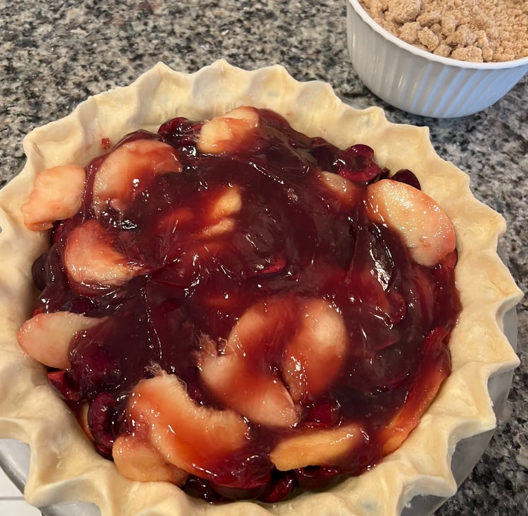 Homemade apple and cherry fruit pie filling in a fluted crust with crumble topping on the side.