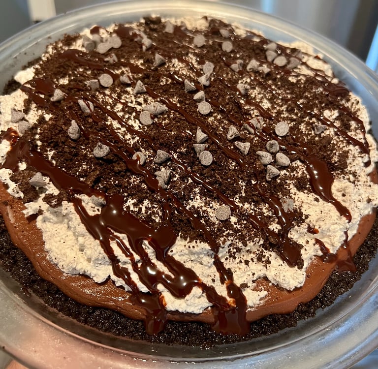 Chocolate silk pie with whipped cream, cookie crumbles, and chocolate drizzle in a glass dish.