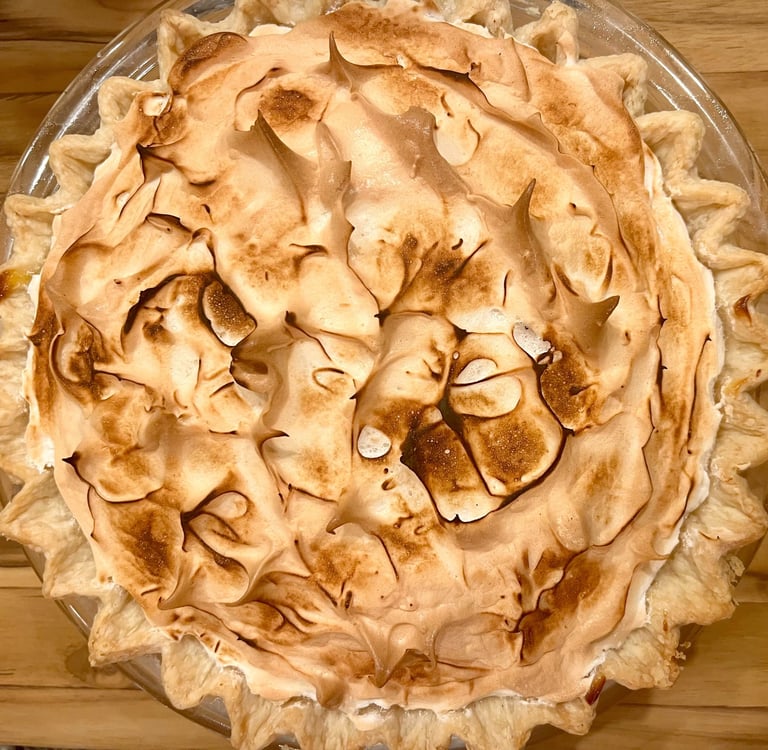 A homemade lemon meringue pie with a toasted golden brown marshmallow topping in a glass baking dish.