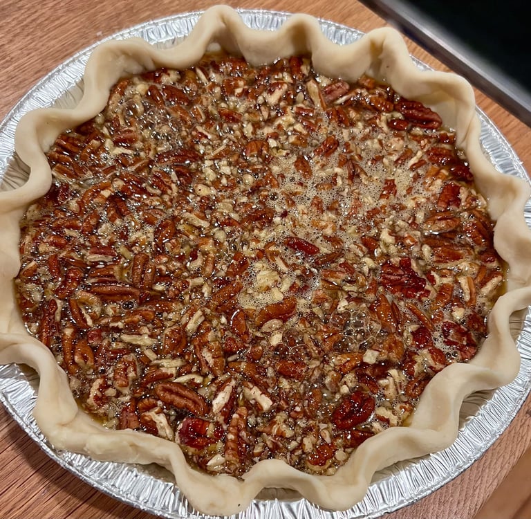 Freshly prepared unbaked pecan pie with a fluted crust in a silver foil tin on a wooden table.