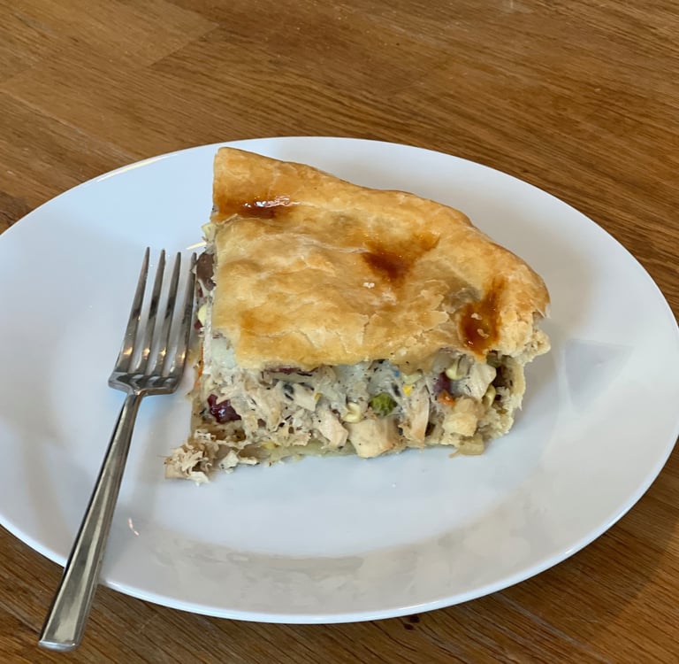 A slice of homemade savory chicken pot pie with a golden flaky crust on a white plate with a fork.