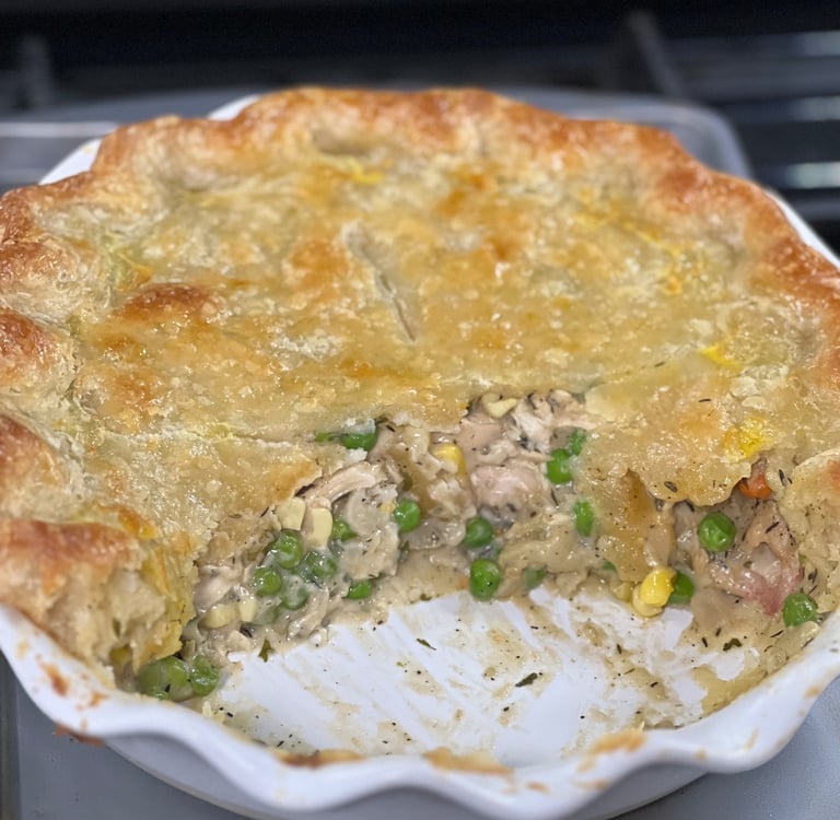 Homemade chicken pot pie with a golden flaky crust, peas, corn, and carrots in a white baking dish.