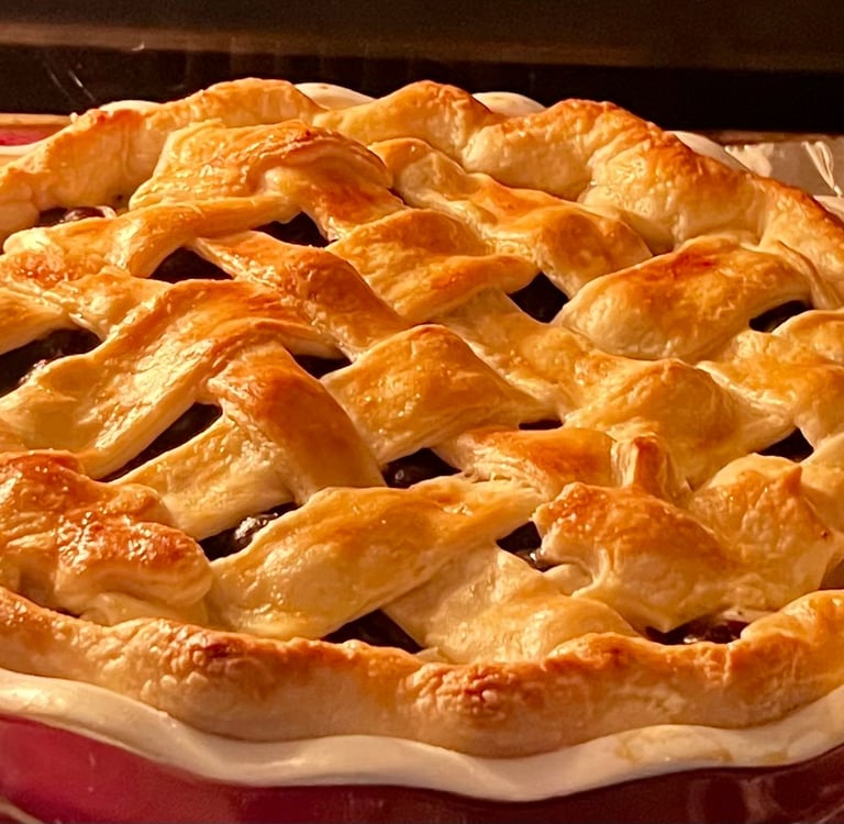 Golden-brown homemade fruit pie with a flaky lattice crust baking in the oven.