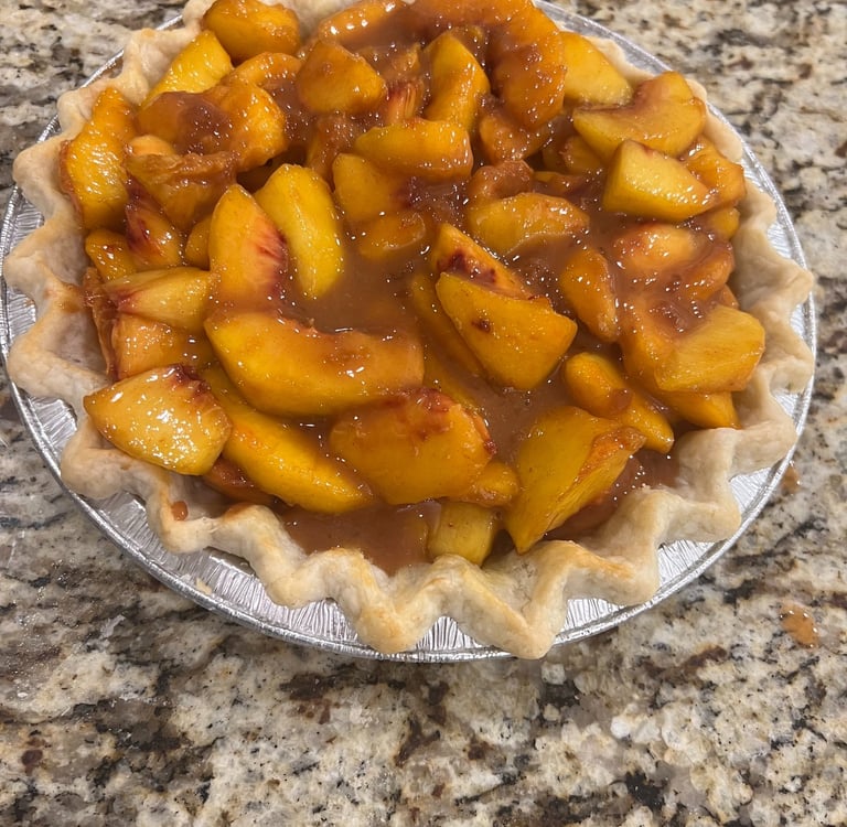 Fresh homemade peach pie with a fluted crust sitting on a granite countertop.