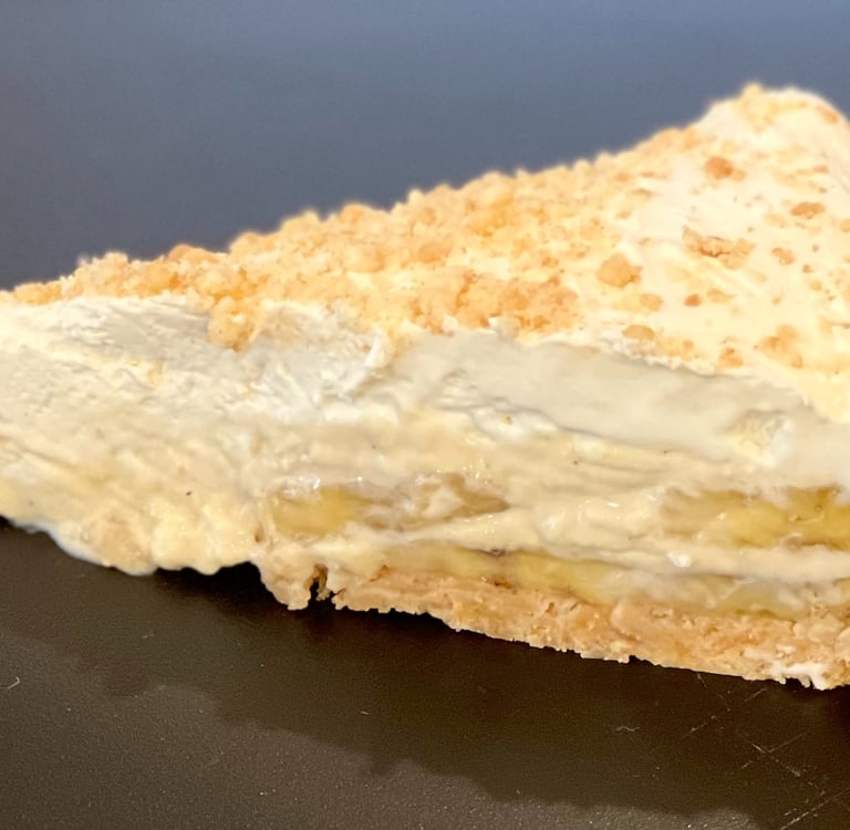 A slice of creamy banana cream pie with a crumbly crust and whipped topping, featuring visible layers of fresh banana and