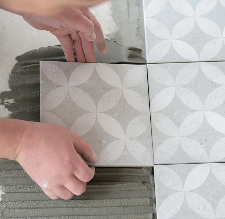 Zbliżenie na płytki, które układa pracownik. Płytki są układane bez fug