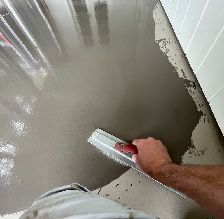 Pracownik rozprowadza masę samopoziomującą za pomocą pacy