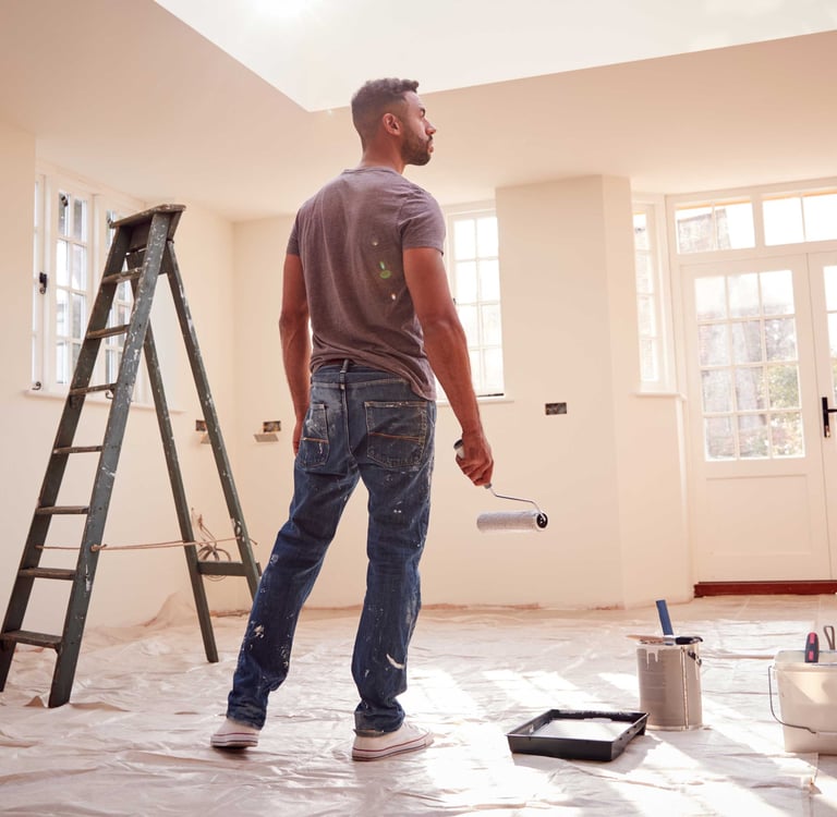Mężczyzna   z wałkiem w ręku stoi na środku pokoju. Ogląda efekt swojej pracy