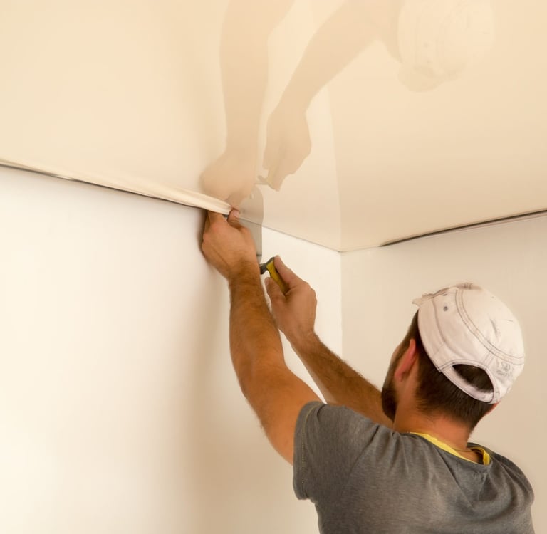 Pracownik napina sufit naciągany i mocuje go do sciany.