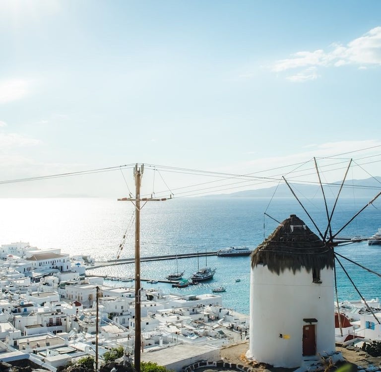 Panoramic view of a traditional white Mykonos windmill overlooking white houses and the Aegean Sea.