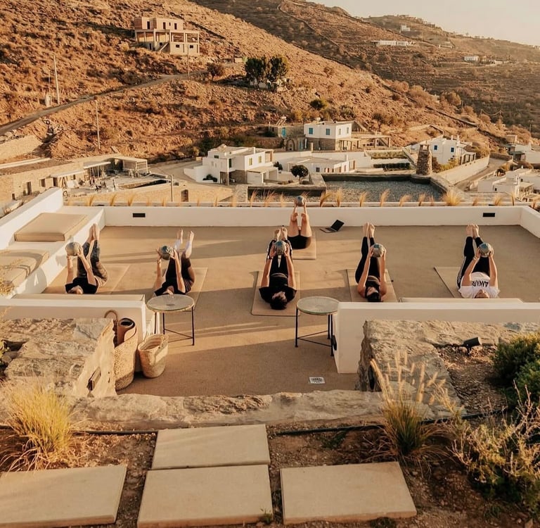 Group pilates class practicing on a sunny rooftop terrace overlooking a scenic mountain valley.
