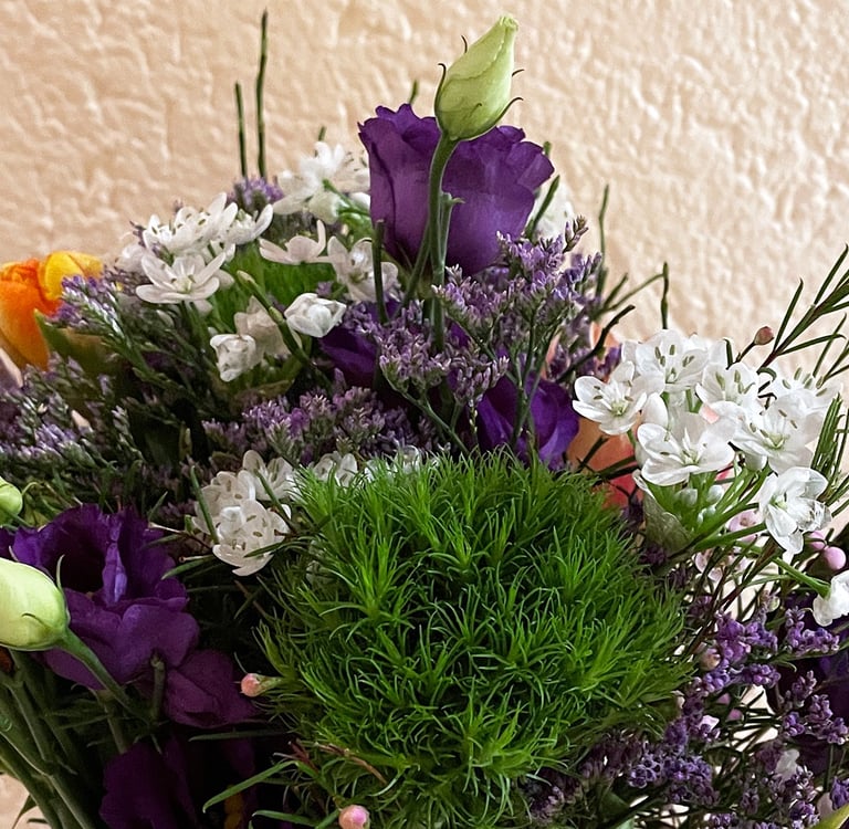 A colorful flower bouquet featuring purple lisianthus, white fillers, and green dianthus.