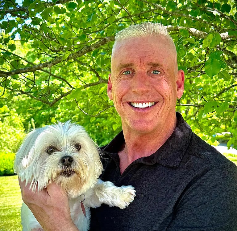 a man in a black shirt is holding a white dog; Tom O'Brien, Owner, Tymeless Properties