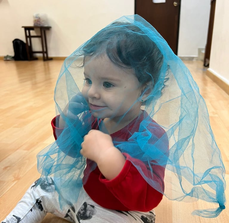 Niña sentada en piso de madera cubierta por una malla azul transparente  en Ukelele Jardín Infantil