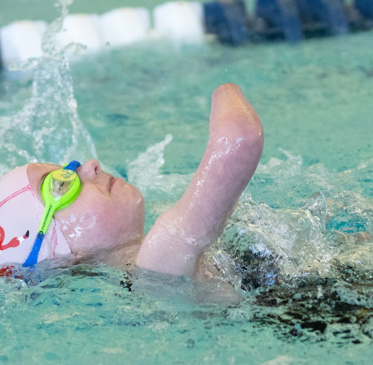 Young girl swimming on her back in pink swim cap with flamingos and blue and green goggles