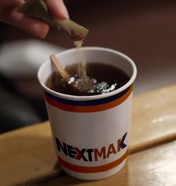 sugar stick pack pouring at a tea cup with NEXTMAK logo